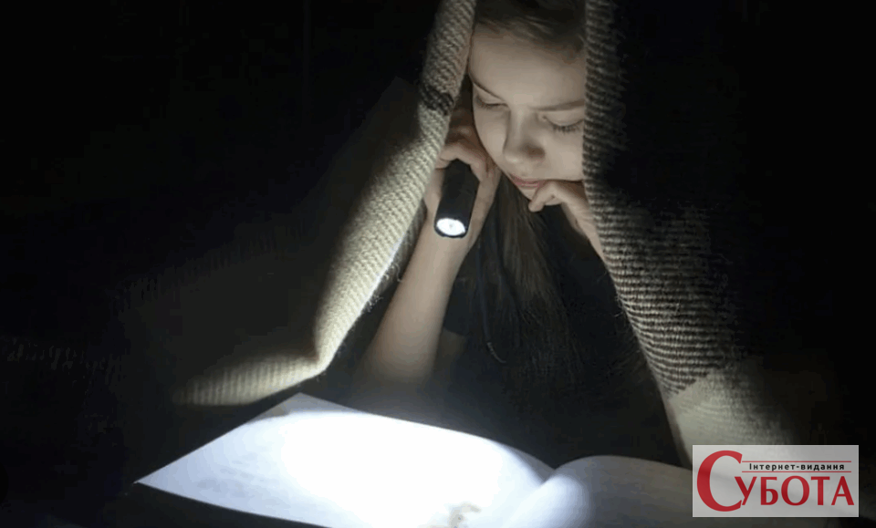 Дитина читає книгу з ліхтариком під ковдрою під час відключення світла