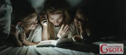 Мати з дітьми читають книгу з ліхтариком під час відключення світла
