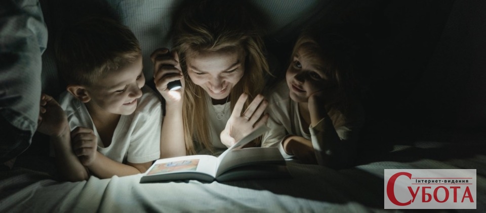 Мати з дітьми читають книгу з ліхтариком під час відключення світла