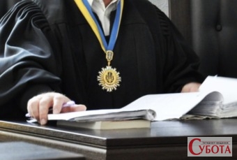Суддя в чорній мантії сидить за столом із матеріалами судової справи