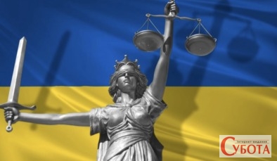 Статуя правосуддя Феміда на тлі прапора України під час суду за державну зраду на Житомирщині