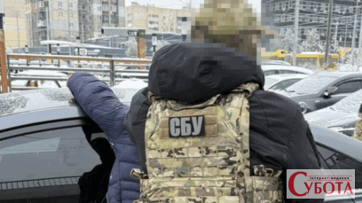 Співробітник СБУ стоїть біля затриманого чоловіка поруч з автомобілем у зимовий час