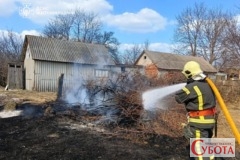 Рятувальник гасить палаючу суху траву та гілля біля будівель на Житомирщині