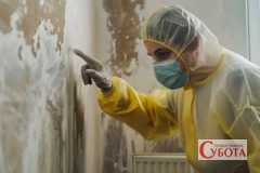 Жінка у захисному одязі оглядає стіну з пліснявою